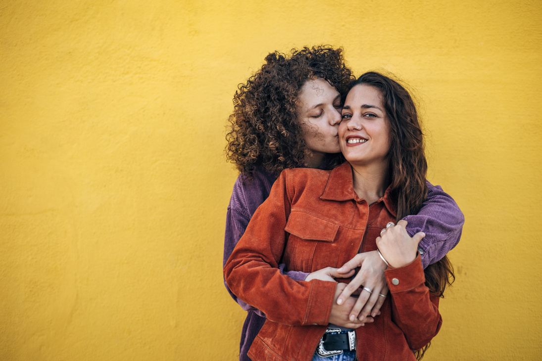 Lesbian Couple Embracing Each Other on Yellow Background
